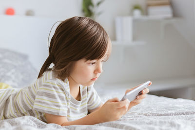  boy lies on the bed and uses a mobile phone. the child plays online games. children and gadgets.