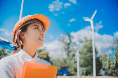 Female engineer in hardhat with file against windmill
