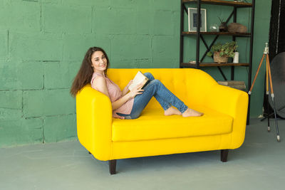 Portrait of woman sitting on chair against yellow wall