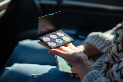 A girl sitting in a car looking at a new palette of eyeshadow. close-up of person using phone. 