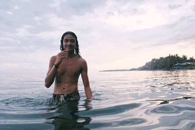 Portrait of shirtless man standing in sea against sky