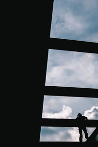 Low angle view of silhouette man standing by window against sky