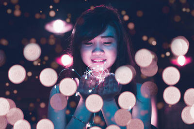 Close-up portrait of smiling young woman holding illuminated christmas lights