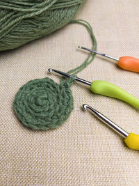 Green yarn thread with and three colorful hooks for knitting and hobbies on gray fabric background.