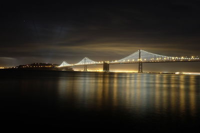 Illuminated bay bridge over river at night