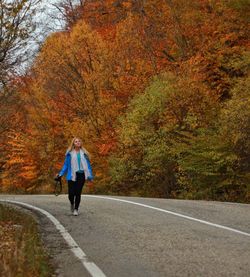 Woman walking with camera on country road against trees during autumn