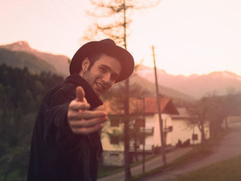 Portrait of young man holding camera against sky