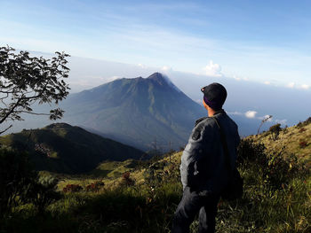 Rear view of man standing on mountain against sky