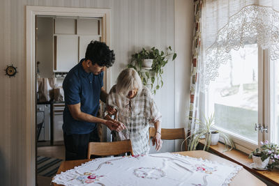 Male healthcare worker assisting senior woman while sitting on chair at home