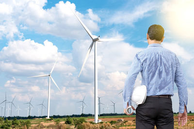 Rear view of man standing by windmill against sky