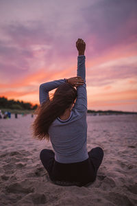 Woman sitting on beach against sky during sunset