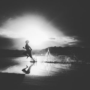 Silhouette person running in water during sunset