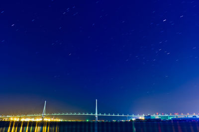 Illuminated bridge against blue sky at night