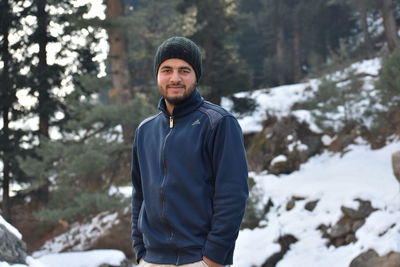 Portrait of young man standing against trees during winter