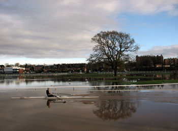 Side view of woman rowing rowboat over lake against cloudy sky