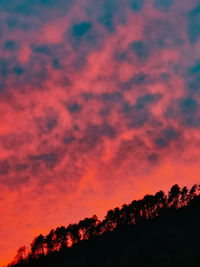 Low angle view of silhouette trees against dramatic sky