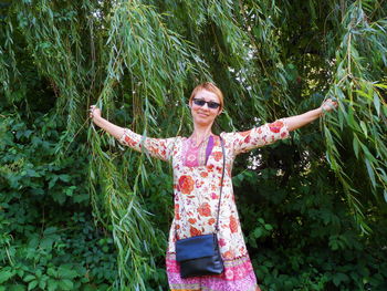 Smiling young woman with sunglasses standing against plants