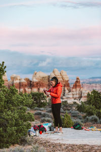 Female camper in orange puffy jacket takes a swig of whiskey in desert