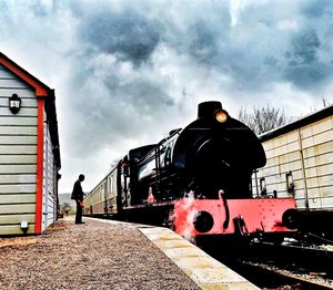 Man standing by train on railroad tracks against sky