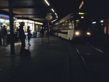 People waiting at railroad station platform at night