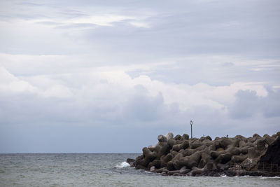 Tetrapod in sea against cloudy sky