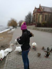 Side view of woman feeding birds on street during winter