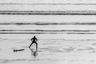 Surfer stretching by surfboard on shore