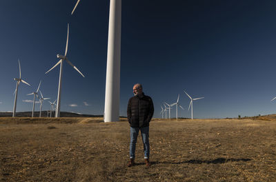 Adult man in winter cloth with modern windmills against blue sky. shot in castilla la mancha, spain