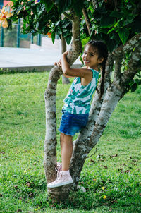Side view portrait of girl smiling while standing on tree at park