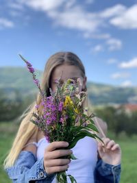 Midsection of woman holding purple flowering plant against sky