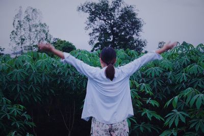 Rear view of woman with arms outstretched standing against plants