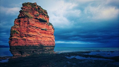 Rock formation on beach against sky