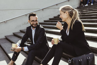 Smiling business people with coffee sitting on staircase