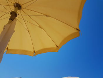 Low angle view of parasol against clear blue sky