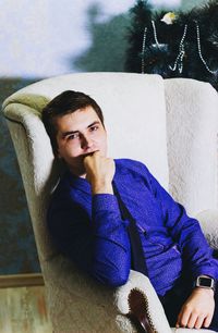 Portrait of man wearing purple shirt relaxing on armchair at home during christmas