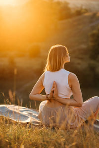 Young woman with folded hands on the back meditating and enjoying beautiful sunset outdoors	
