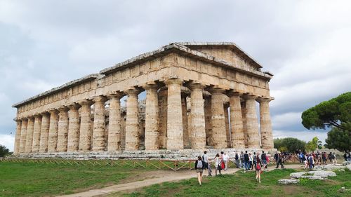 Tourists at historical building against cloudy sky