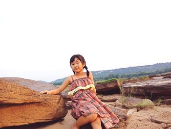 Portrait of girl sitting on rocks against clear sky