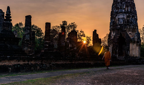 Monk walking at historic temple against sky during sunset