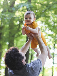 Caucasian young dad throws up his hands to his little daughter in a yellow bodysuit