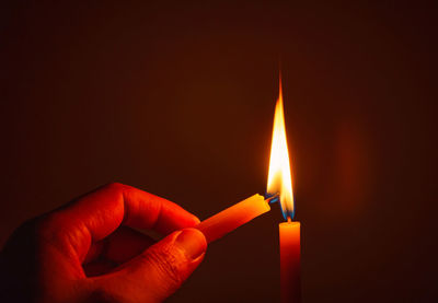 Close-up of hand igniting candle in darkroom