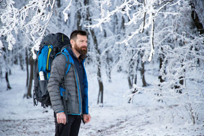Mature man with backpack standing against snow covered trees during winter
