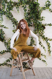 Portrait of young woman sitting on chair against plants