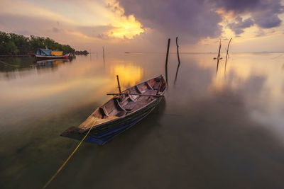 Boat moored in water against sky during sunset