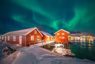 Houses by illuminated buildings against sky at night during winter