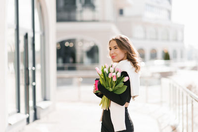 Young woman with tulips and cup of coffee on city street