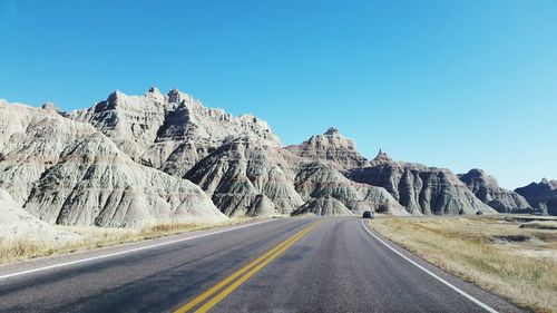 Empty road by mountains against clear sky