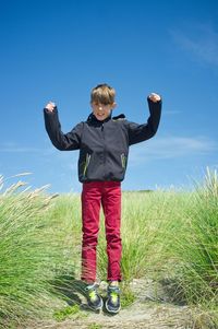 Full length of woman standing on grassy field against blue sky