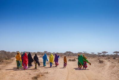 Rear view of women wearing scarfs while walking in desert against sky