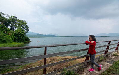 Girl standing byv railing near lake